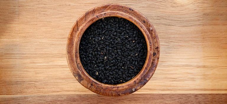 Schwarzkümmelsamen in brauner Holzschale auf Holztisch