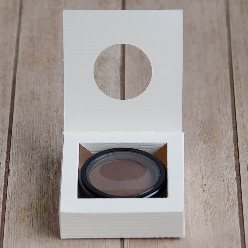 Geöffneter Verpackungskarton mit Eyeshadow auf Holztisch.